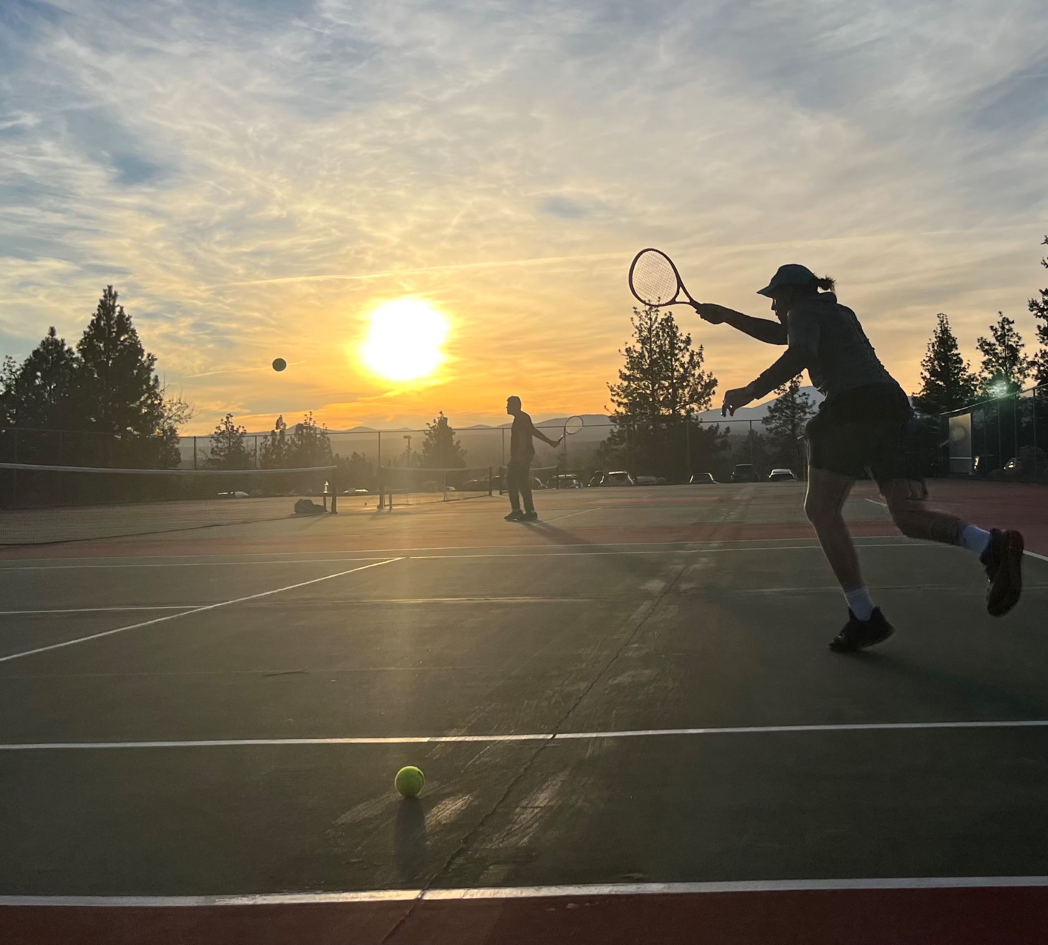 people playing tennis with sunset and mountains in the background