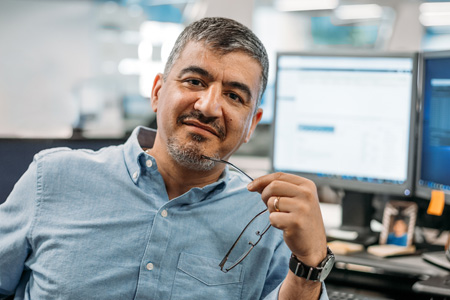 Male business admin with greying hair and beard in front of comuter monitors