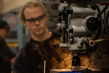 A student operating a machine as sparks fly from metal, focused on machining work in a workshop.