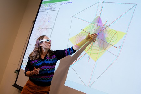 A COCC math instructor wearing 3D glasses points to a three-dimensional graph projected on a large screen during a calculus lecture.