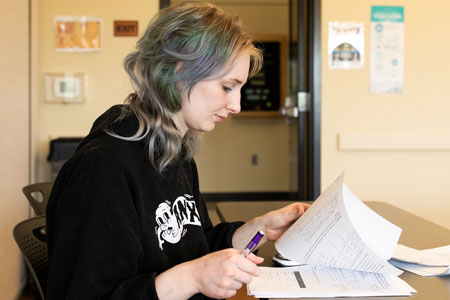 A student reviews handwritten math papers at a desk, pen in hand.