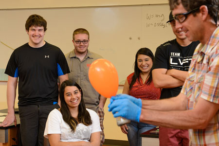 Career minded Physics students happily watching instructor inflate an orange balloon